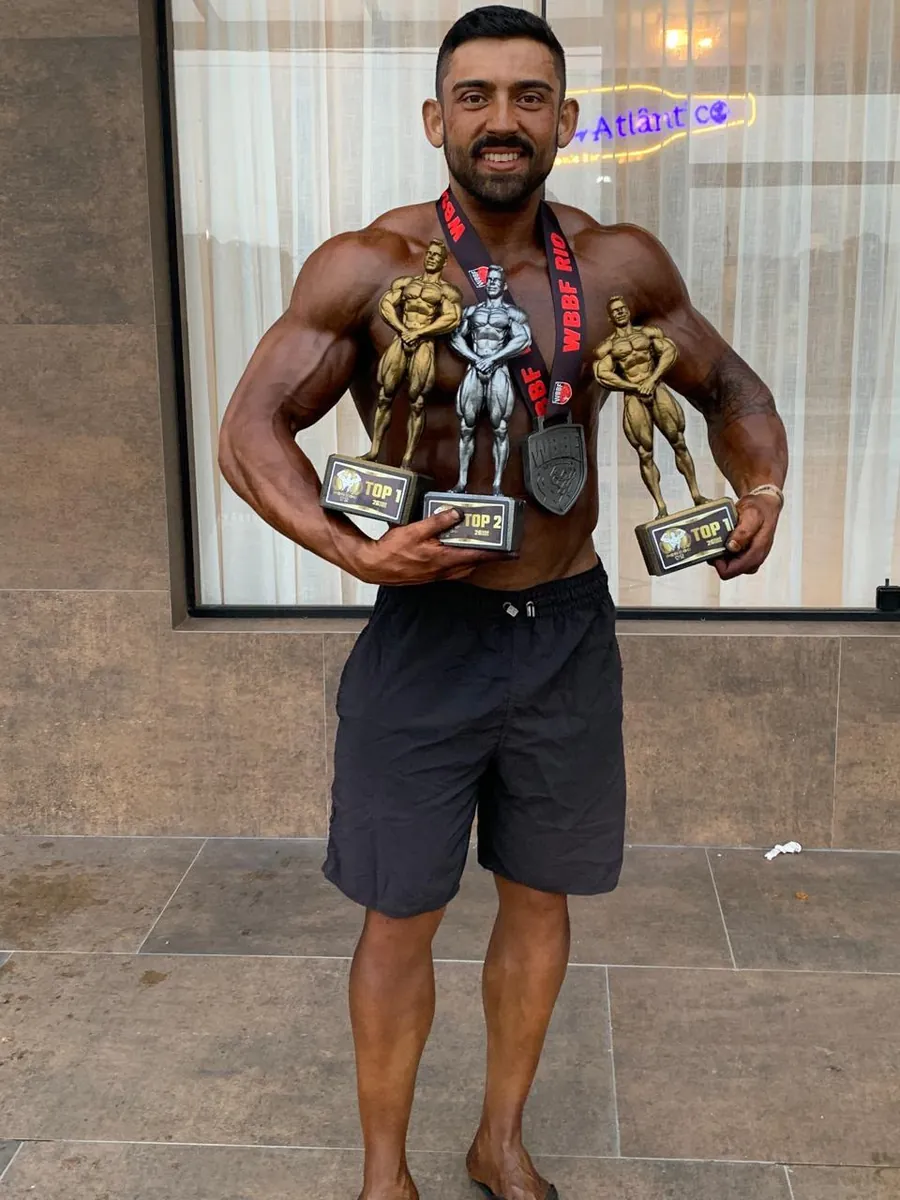 Nutricionista Lucas com troféus e medalha de competição de fisiculturismo
